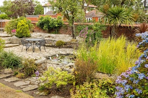 A garden with a stone patio, a small pond, and various plants and flowers.