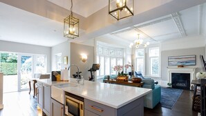 A spacious kitchen with a large island, modern appliances, and a dining area with a blue sofa and fireplace. - Tranquil Apartment in Merseyside (Liverpool)
