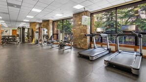 A gym with treadmills, weight machines, and a stone wall.