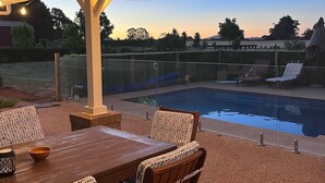 An outdoor patio area with a wooden table and wicker chairs, overlooking a swimming pool. - Pet friendly country retreat (Tylden)