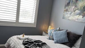 A bedroom with a bed, a window with blinds, a painting on the wall, and a lamp on the nightstand. - Pet friendly country retreat (Tylden)