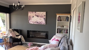 A modern living room with a grey sofa, a large floral painting, a bookshelf, and a chandelier. - Pet friendly country retreat (Tylden)