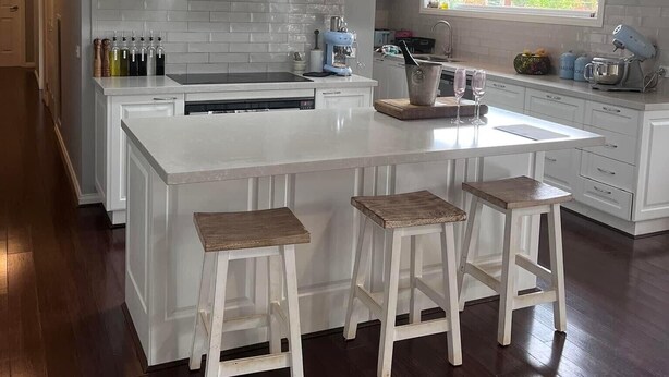 A modern kitchen with white cabinetry, a central island with stools, and a window with a view of greenery. - Pet friendly country retreat (Tylden)