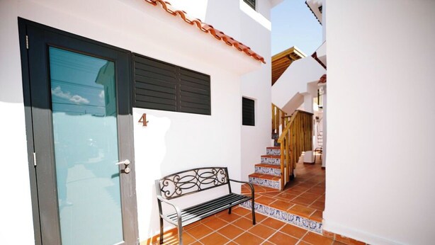 A narrow outdoor corridor with a bench, a door, and a staircase.