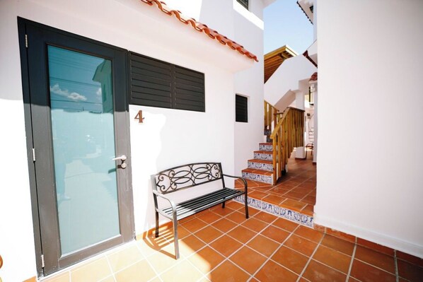 A narrow outdoor corridor with a bench, a door, and a staircase.