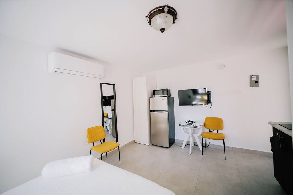 Een kleine hotelkamer met een bed, een kitchenette, een televisie en twee gele stoelen.
