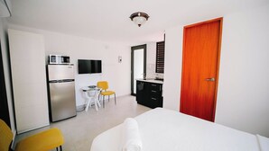 A hotel room with a bed, a desk, a chair, a television, a refrigerator, and a door.