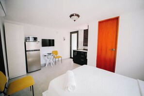 A hotel room with a bed, a desk, a chair, a television, a refrigerator, and a door.