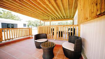 Un patio exterior con barandillas de madera, dos sillones de mimbre con cojines y una pequeña mesa redonda.