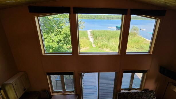 Una habitación con amplios ventanales que dan a un lago, techo de madera y vista a un muelle.