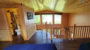 Una habitación con pisos de madera, un balcón con barandilla de madera, un cuadro en la pared y vistas al exterior.