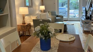 A cozy living room with a wooden dining table, a blue vase with white flowers, a sofa, and a chair.