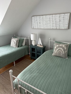 A bedroom with two single beds, a nightstand with a lamp, a decorative sailboat, and a wall art piece.