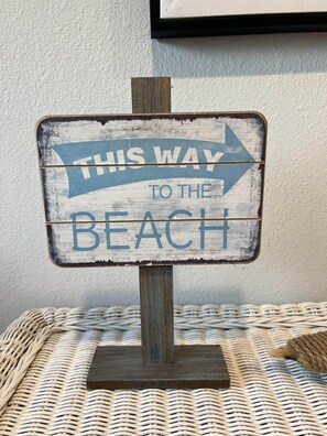 A rustic wooden sign with a blue arrow pointing right, reading "THIS WAY TO THE BEACH."