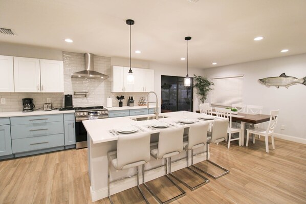 A modern kitchen with white cabinets, a central island with bar stools, and a dining area with a wooden table and chairs.