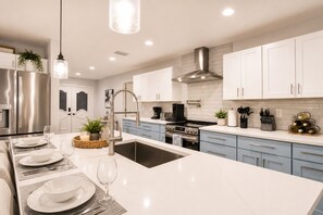 A modern kitchen with white cabinets, stainless steel appliances, and a central island with seating. - 10 mins to AMI/IMG - 4/Bd Pool Home (West Bradenton)
