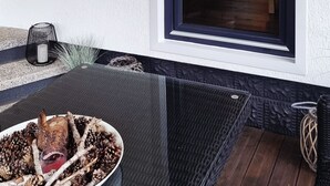 Zona relax esterna moderna con tavolino in vetro, lampada pendente in vimini e vista su un giardino attraverso un'ampia finestra.