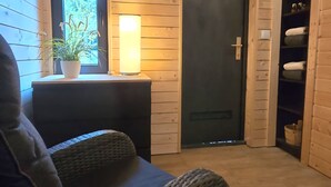 Una stanza accogliente con un divano in vimini, un tavolino con una lampada, una pianta in vaso e una porta in legno.