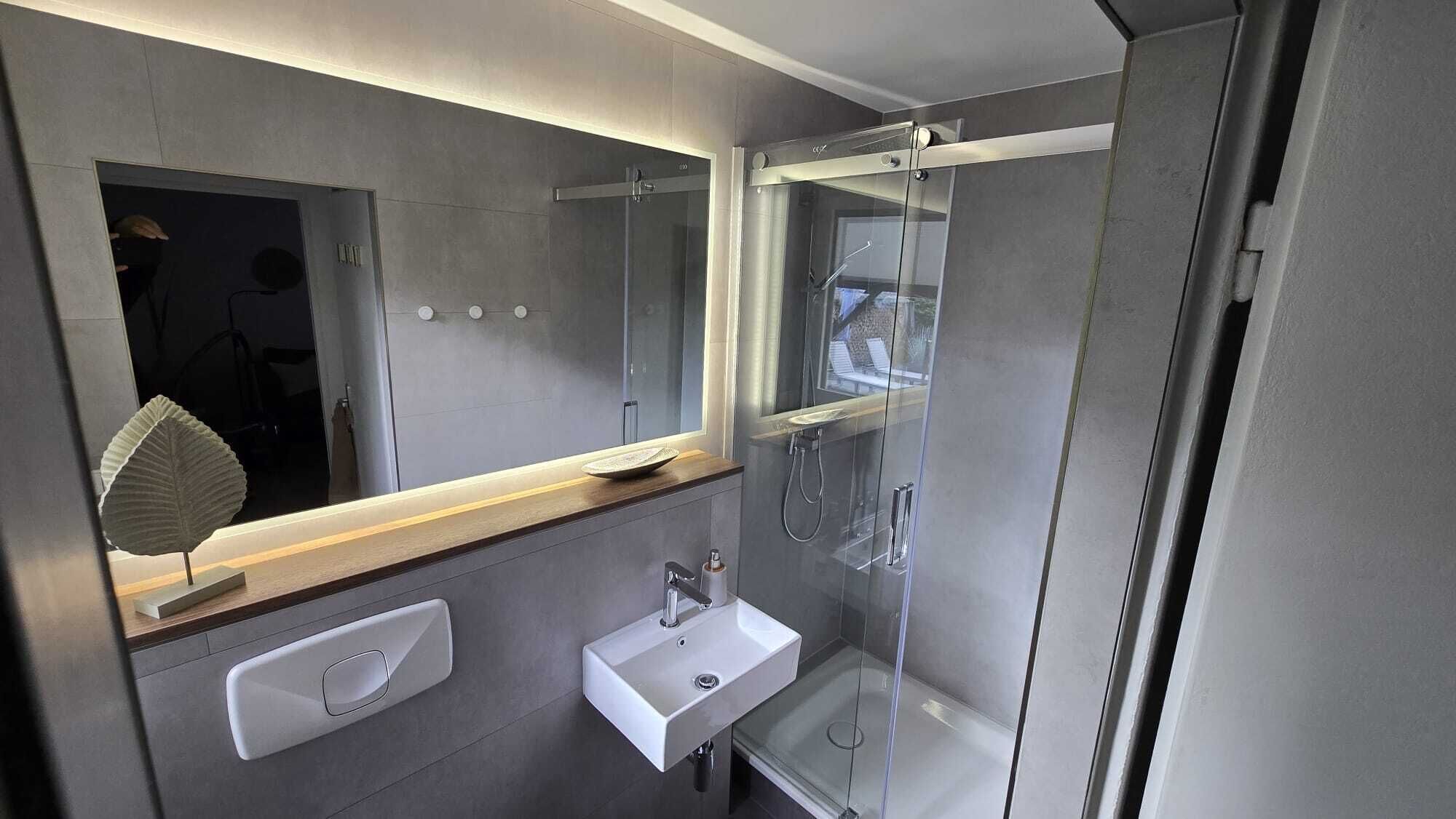 A modern bathroom with a large mirror, a sink, and a glass-enclosed shower.