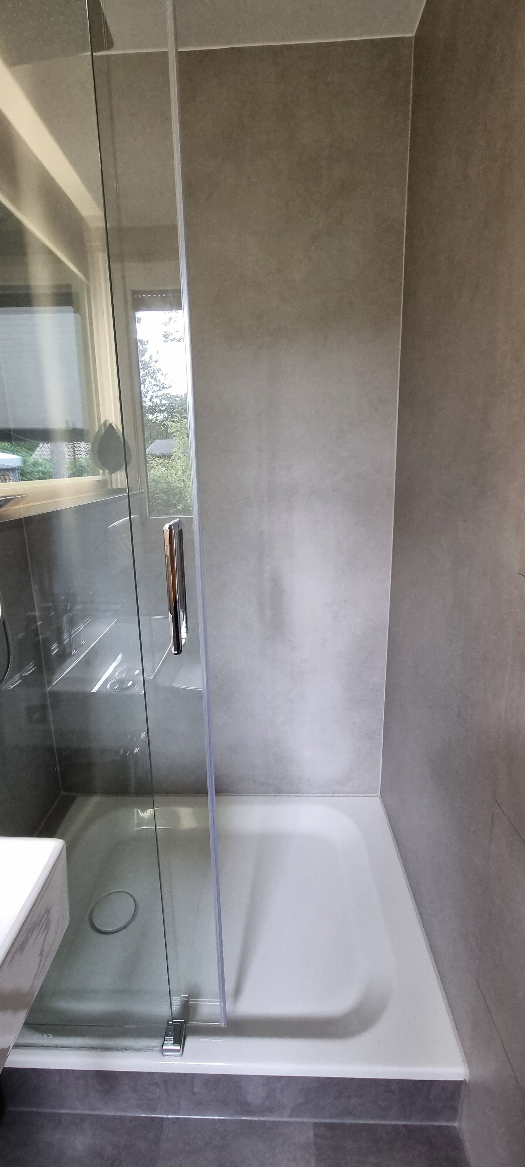 Une salle de bain moderne avec une douche à l’italienne en verre, une baignoire blanche et des carreaux gris.