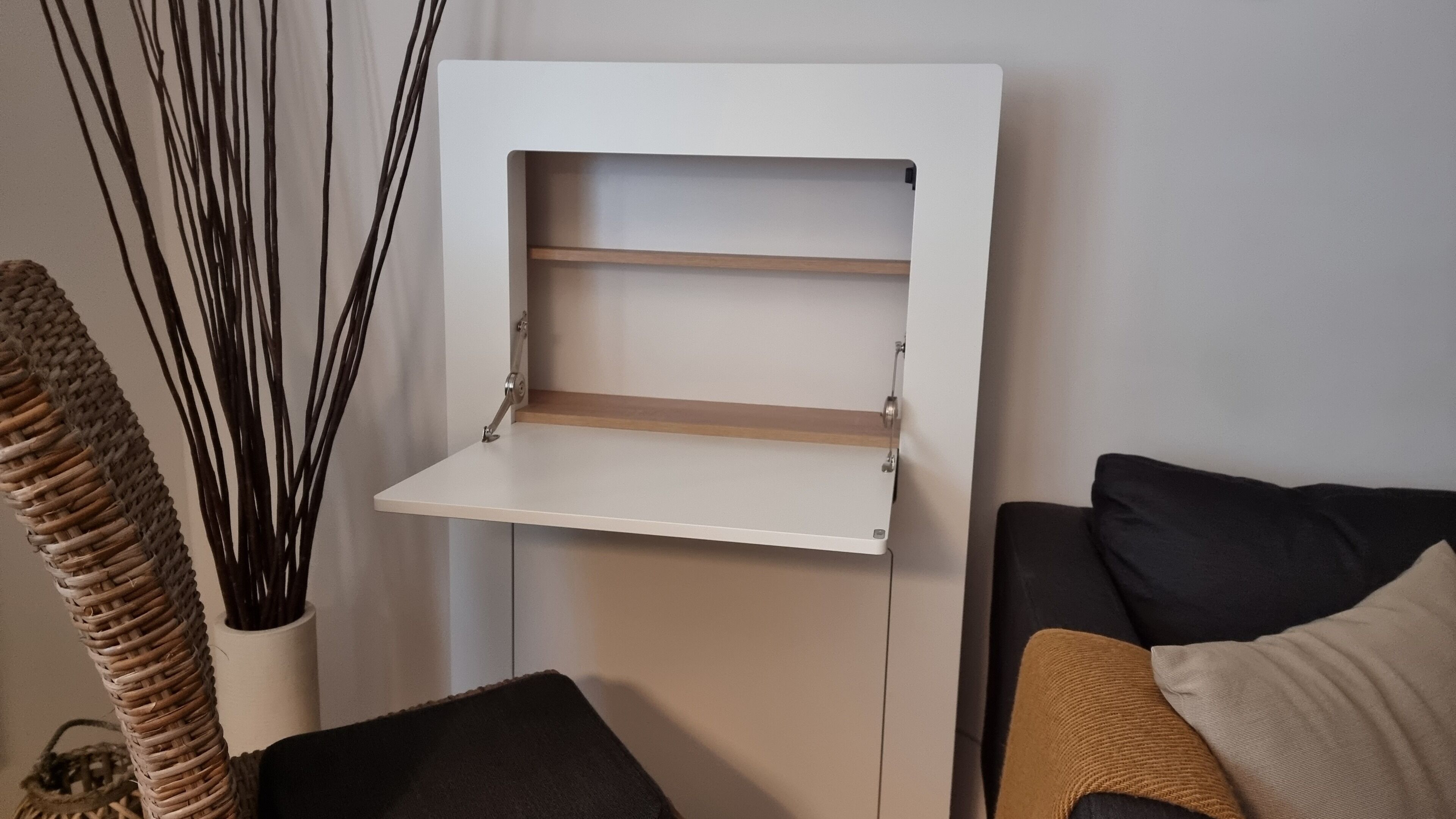 A white shelf unit with two shelves, a woven basket, and a black cushion.