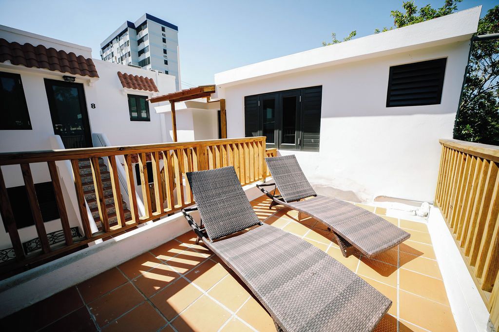 Una terraza en la azotea con dos tumbonas, una barandilla de madera y vistas a un edificio con tejado de tejas y una puerta marcada con el número 8.