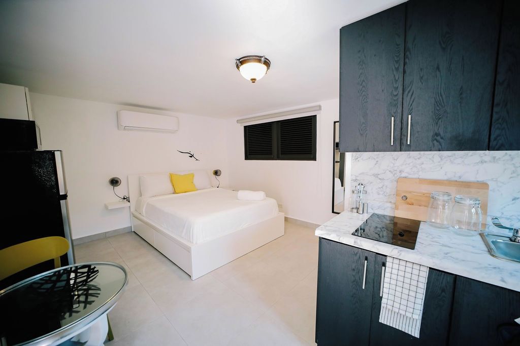 Una habitación compacta con una cama, un pequeño kitchenette y una mesa de vidrio.