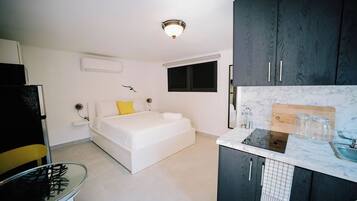Una habitación compacta con una cama, un pequeño kitchenette y una mesa de vidrio.
