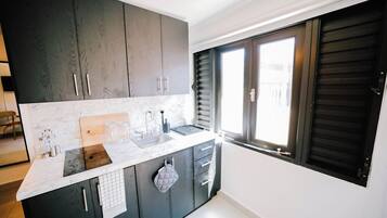 Una cocina moderna con armarios oscuros, encimera de mármol y ventana con contraventanas.
