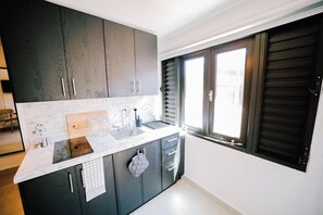 A modern kitchen with dark cabinets, a marble countertop, and a window with shutters.