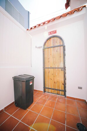 A closed wooden gate with an EXIT sign above it, a black trash bin to the left, and a tiled floor.