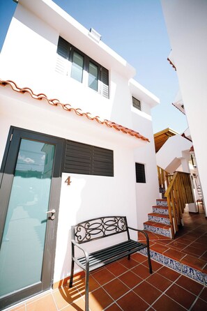 A white building with a black door, a bench, and a staircase with patterned tiles.