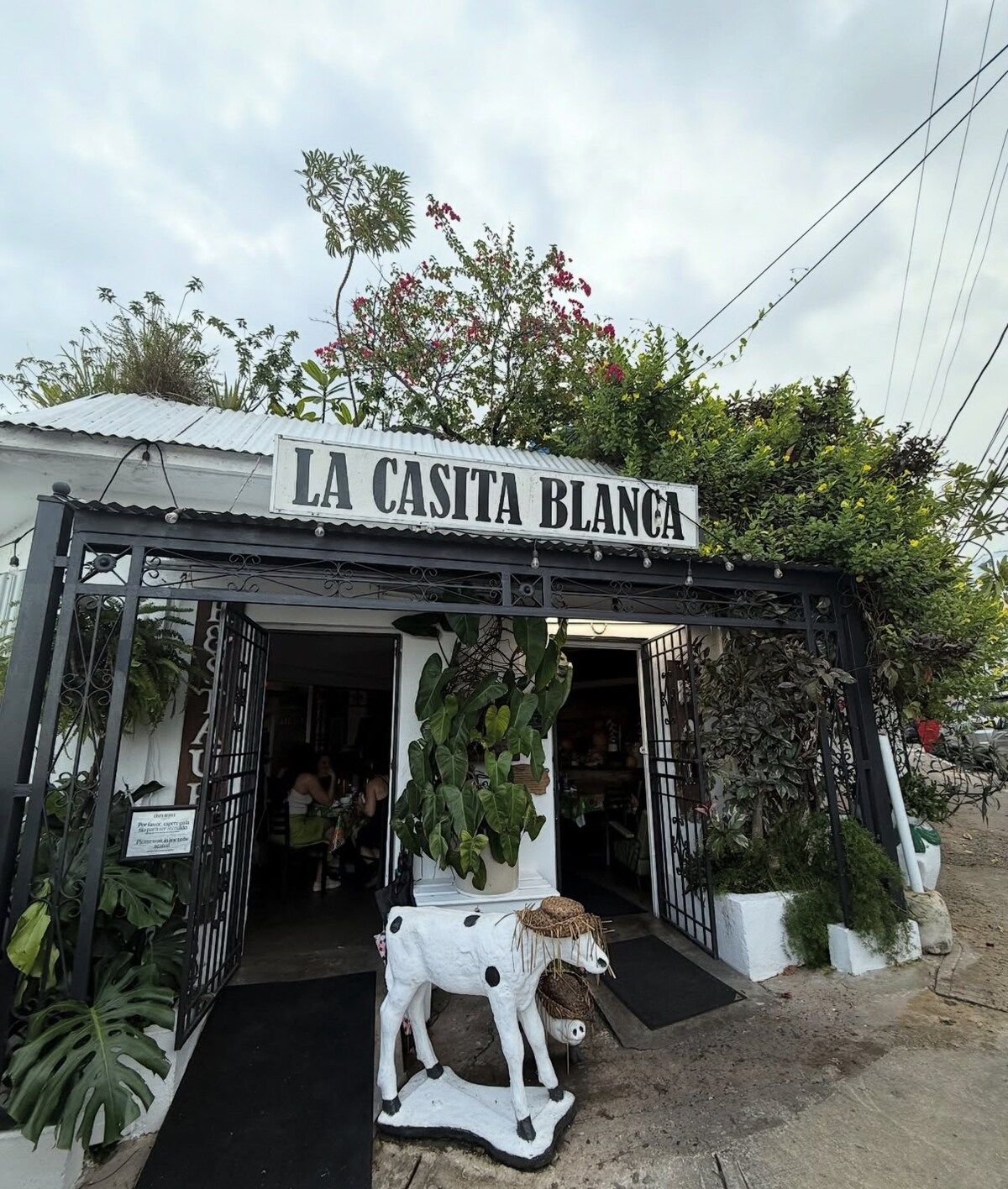 Ein Geschäft mit einem Schild, das 'LA CASITA BLANCA' zeigt, und einer dekorativen Kuhstatue vor der Tür.
