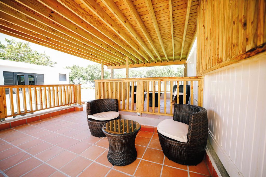 Eine Terrasse im Freien mit Holzwerteln, zwei Korbstühlen mit Kissen und einem kleinen runden Tisch.