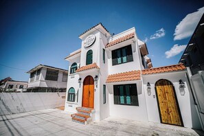 A two-story building with a white facade, a wooden door, and a sign that reads 'Casa Sagrado.'
