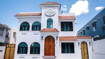 Un edificio de dos pisos con un letrero que dice 'Casa Sagrado'. Tiene un techo de tejas, ventanas arqueadas y una puerta de madera central.