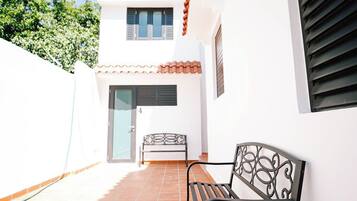 Un patio con un banco de metal negro y una mesita, paredes blancas y piso de baldosas.