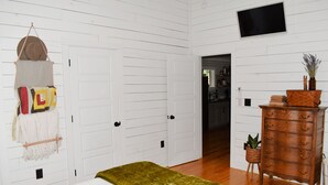 Une chambre à coucher comprenant un lit, une commode, un téléviseur et un couloir menant à une autre pièce.