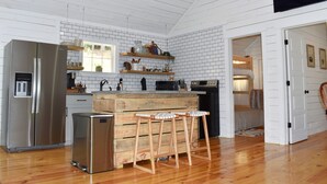 Une cuisine dotée d’un îlot central en bois, d’appareils électroménagers en acier inoxydable et d’un dosseret en briques blanches.