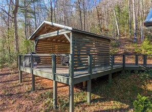 A wooden cabin with a fenced deck, surrounded by trees.