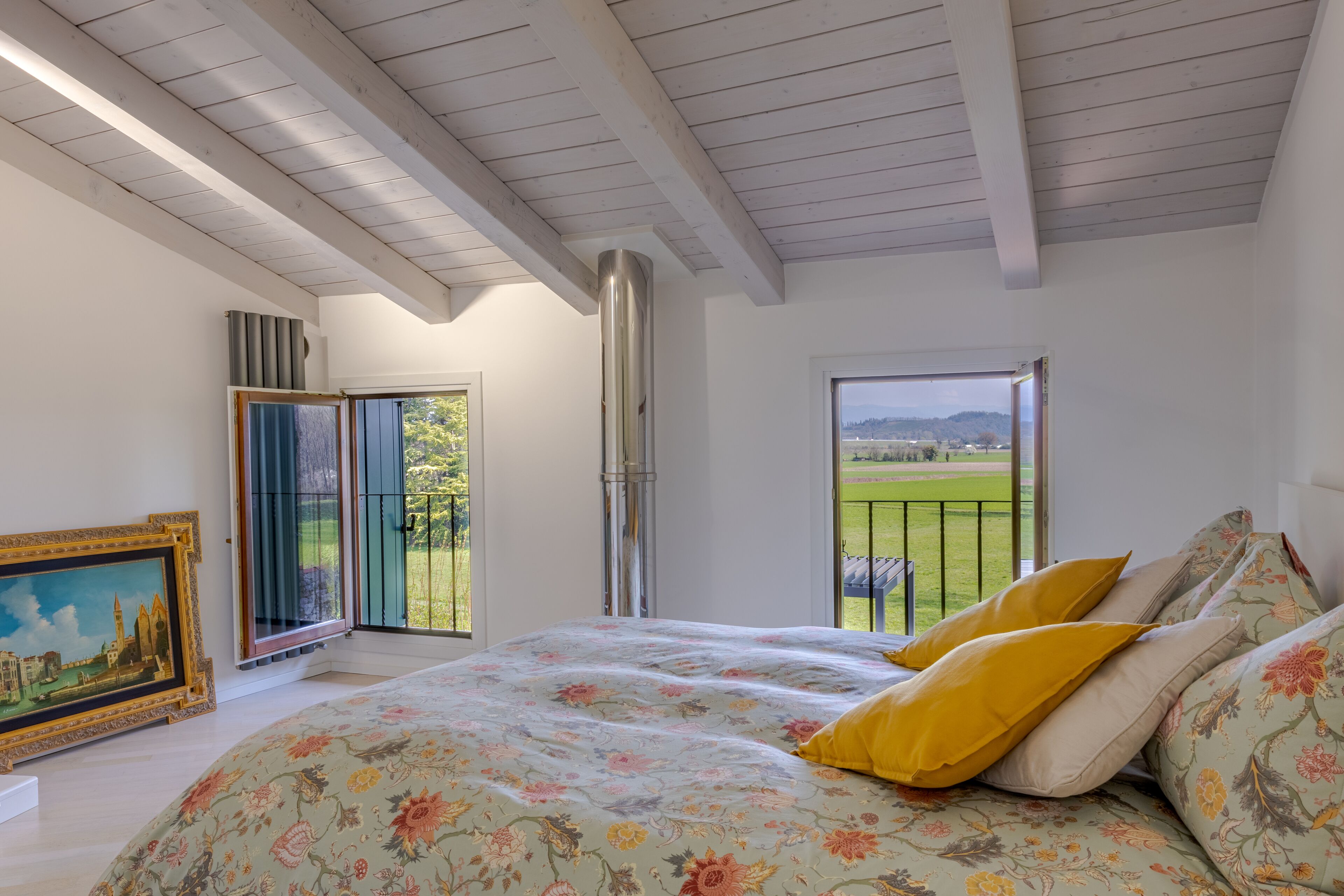 Quarto com cama grande, pintura na parede e varanda com vista para o campo.