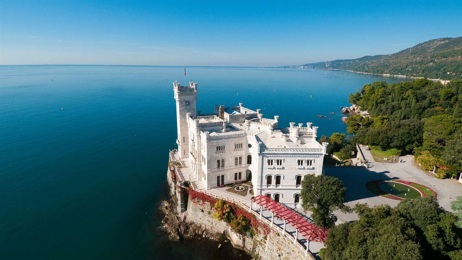 A large, white castle-like building with multiple towers, situated on a cliff overlooking a calm sea.