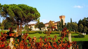 Un bâtiment historique doté d’une tour, entouré de jardins bien entretenus et d’un grand arbre.