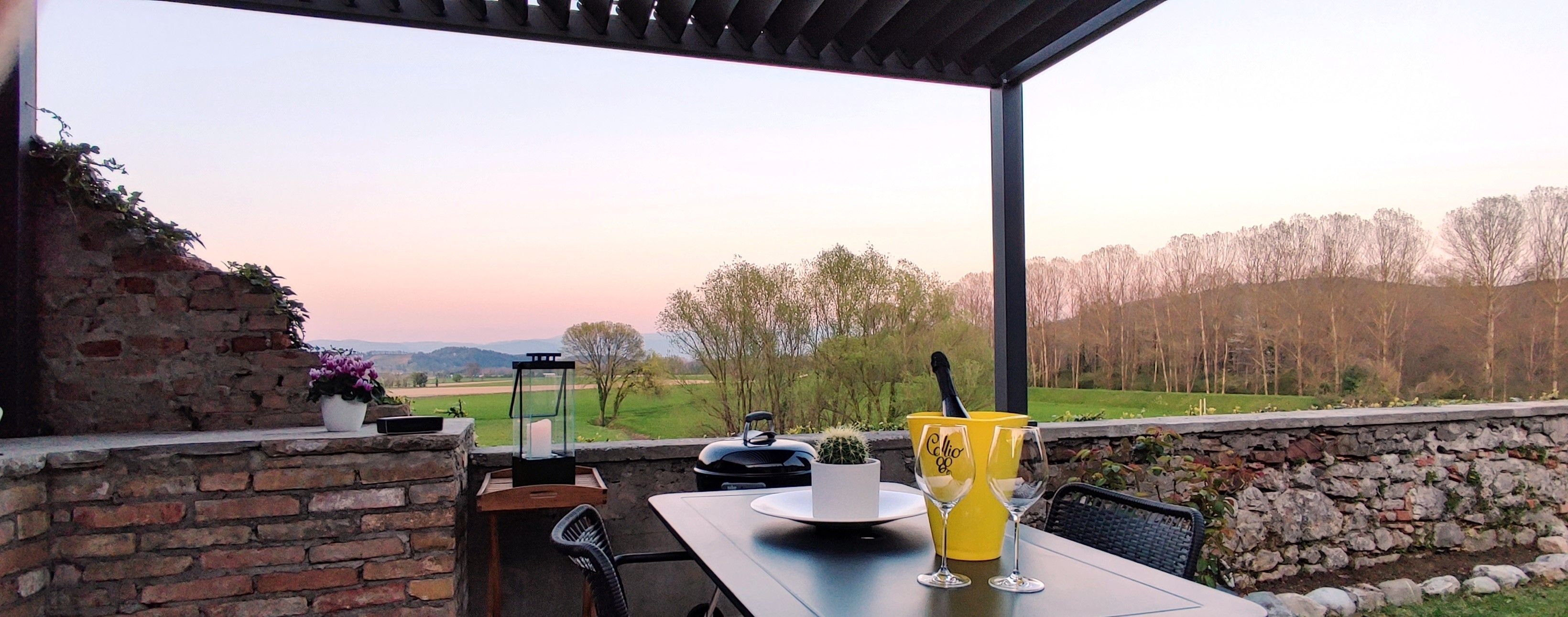 Un patio al aire libre con una mesa, sillas, un farol y vistas al campo.