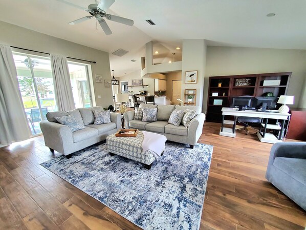 A spacious living room with a large sofa set, a coffee table, and a desk with computers.