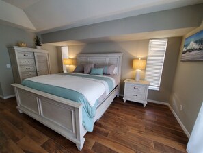 A bedroom with a large bed, a nightstand, a dresser, and a window with blinds.
