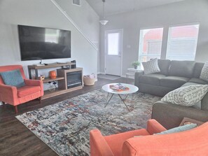 A living room with a flat-screen TV, a sofa, a chair, a coffee table, and a patterned rug.