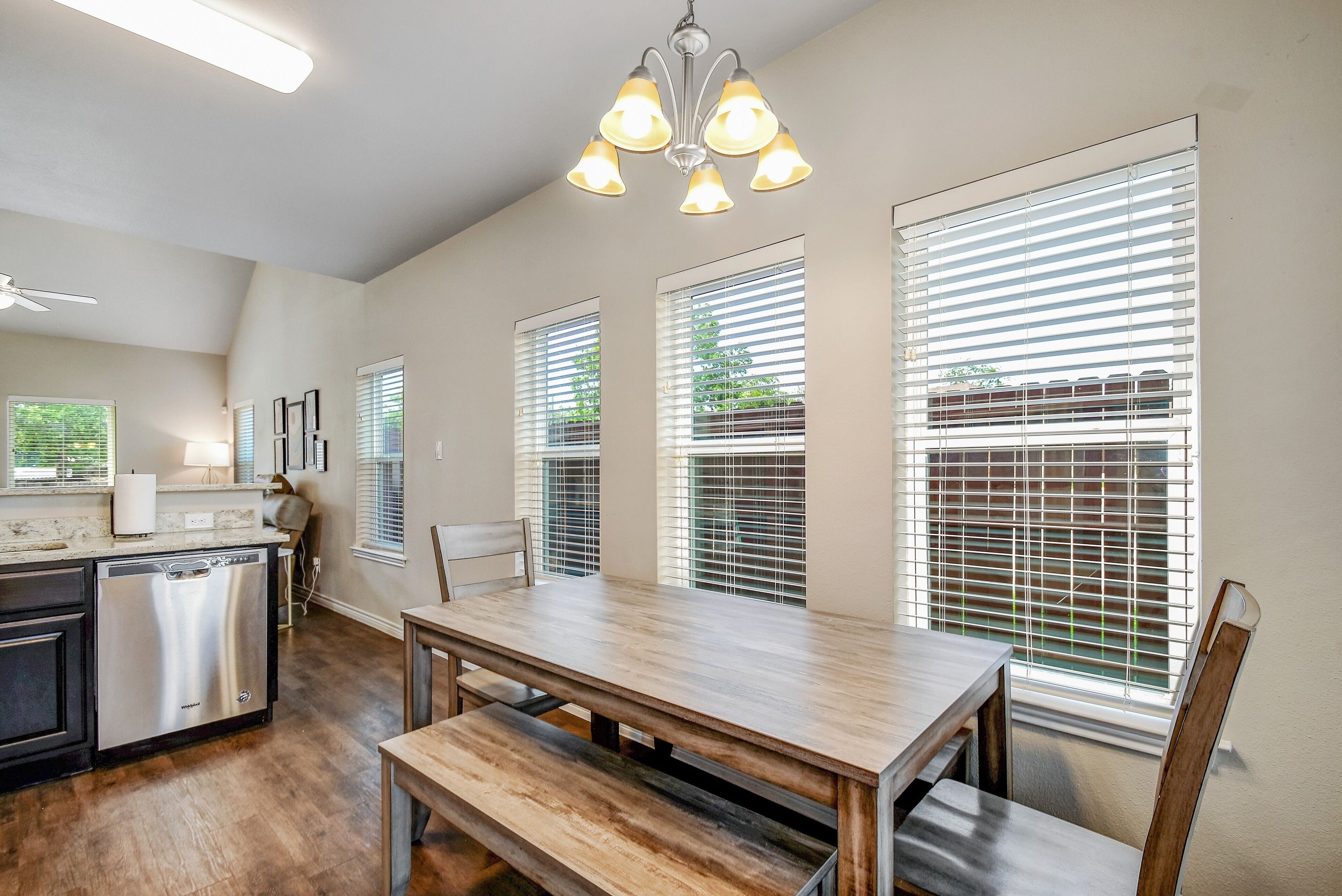 Una cocina amplia con una mesa y banco de madera, lavavajillas y ventanas grandes con persianas.