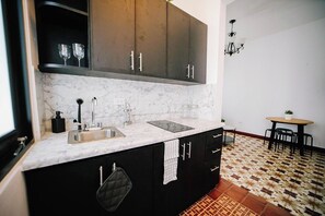 Una cocina con armarios oscuros, encimera de mármol, fregadero y comedor con mesa y sillas.