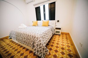 A bedroom with a bed, a nightstand, and a window with shutters.